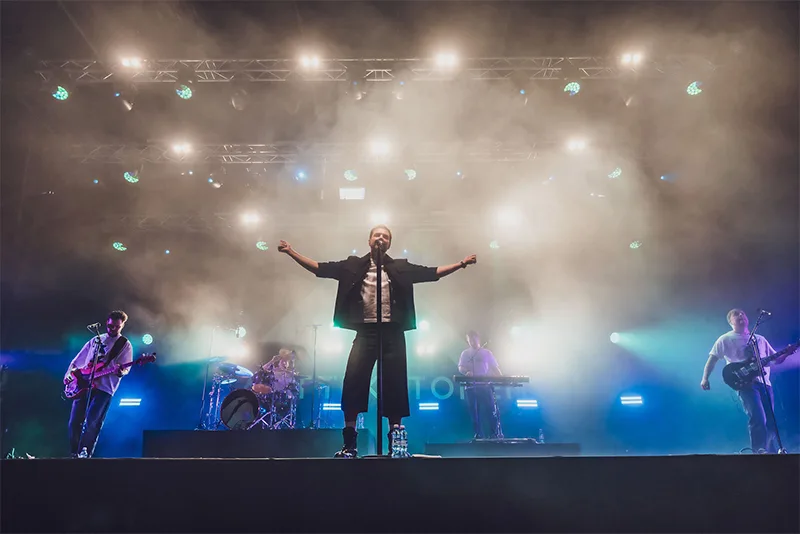 Live concert stage lighting design featuring bright white beams and dramatic backlighting behind singer Antti Ketonen and his band.