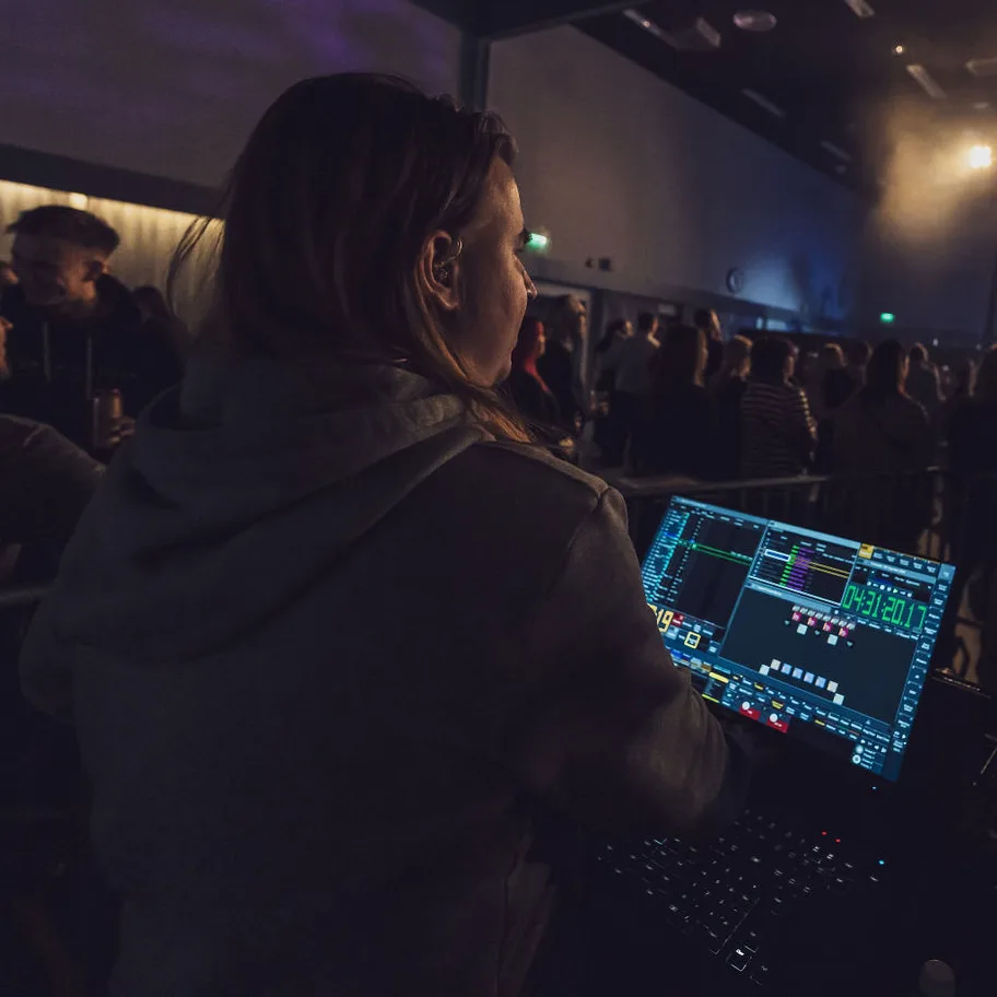 Finnish lighting designer operating a grandMA3 lighting console and running show automation during a live concert performance.