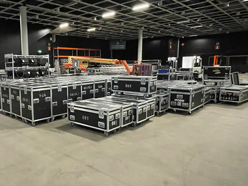 Large-scale event production setup in an arena showing rows of lighting and technical equipment flight cases ready for stage assembly.